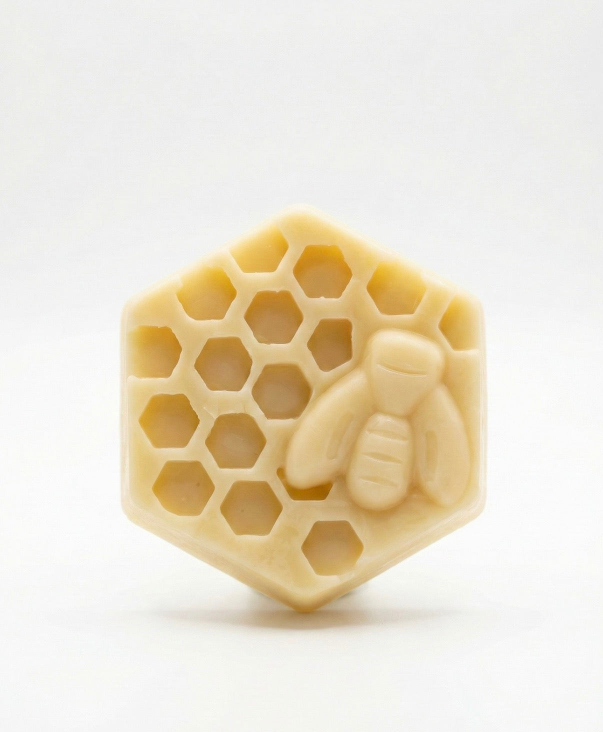 Close up of The Hive Bar by Small Town Honey Co sitting on a white marble slab. A solid hexagonal beeswax massage bar with a detailed 3D honey bee molded on top.