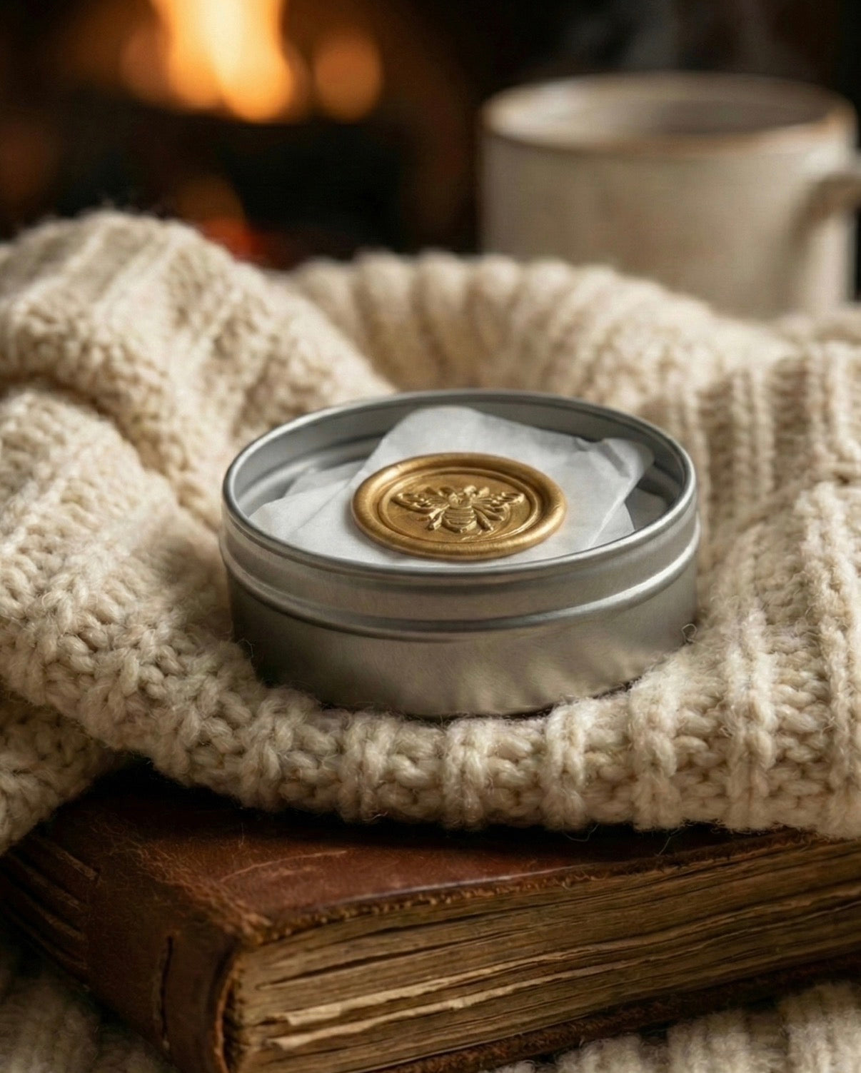 Cozy winter lifestyle scene. The Hive Bar in its silver tin sitting on a chunky knit beige sweater next to a rustic leather journal. Perfect gift for self-care and travel.