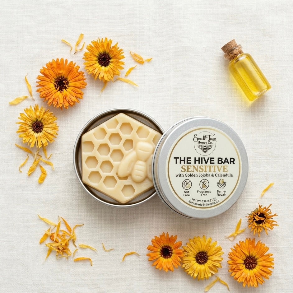 The Hive Bar Sensitive waterless lotion in a tin with honeycomb design, surrounded by yellow flowers on a light background.
