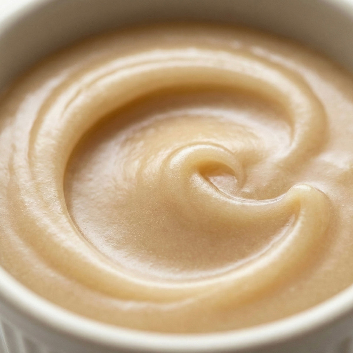 Macro close up texture of smooth creamed honey in a ramekin showing velvet swirls and grain-free consistency.